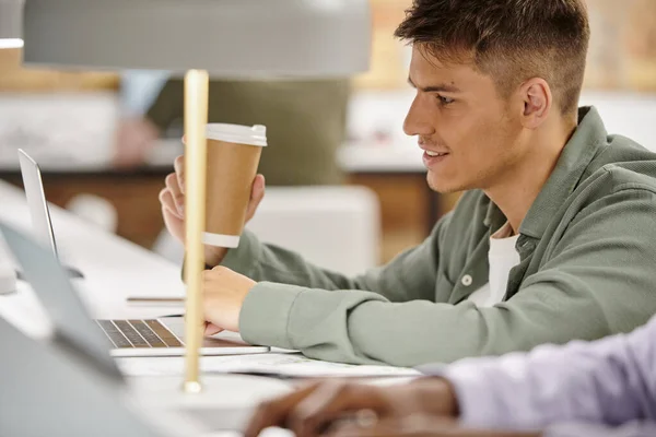 Homme heureux tenant café pour aller et en utilisant ordinateur portable, environnement de bureau, coworking, projet de démarrage — Photo de stock