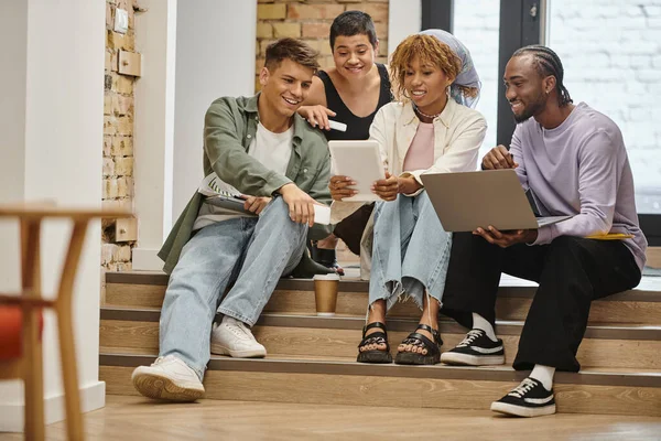 Equipo diverso feliz mirando tableta, sosteniendo gadgets, sentado en escaleras en coworking, puesta en marcha — Stock Photo
