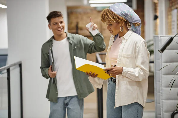 African american woman looking at folder, young man gesturing in modern office, startup project — Stock Photo