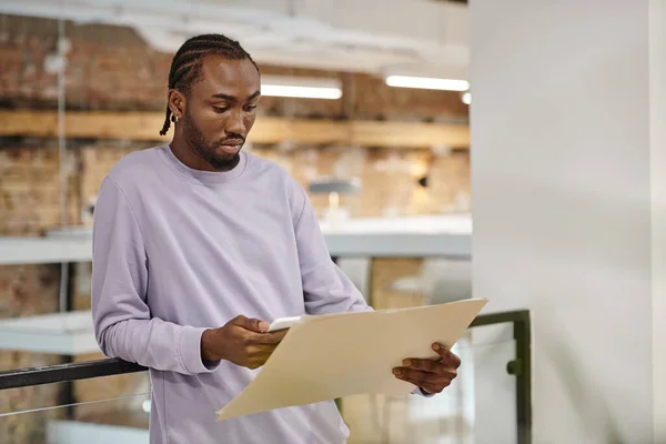 Homem americano africano olhando para o projeto no papel, usando smartphone, planejamento, estratégia, digital — Fotografia de Stock