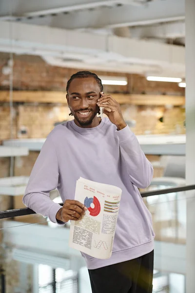 Happy african american man talking on smartphone, planning, startup, holding graphs, smile — Stock Photo