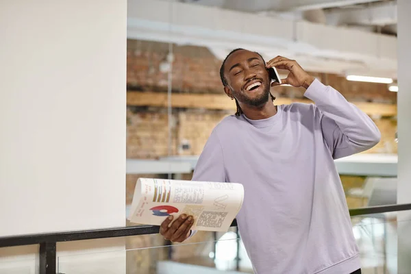 Joyful african american man talking on smartphone, laughing, startup, holding graphs, digital — Stock Photo