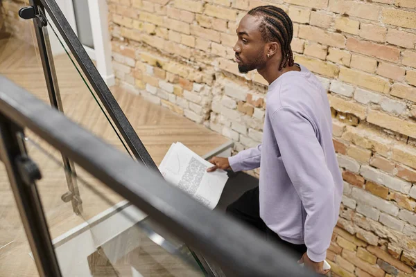 Jovem afro-americano homem segurando gráficos, andando em escadas em co-working, gen z, startup, negócios — Fotografia de Stock
