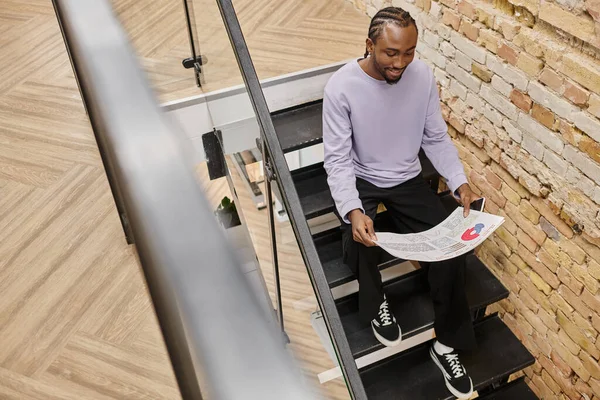 Freudiger afrikanisch-amerikanischer Mann mit Grafiken, sitzt auf Treppen in Coworking, Gen Z, Start-up, Business — Stockfoto