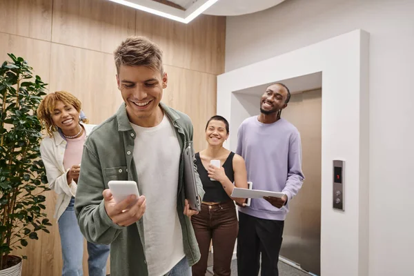Cheerful young man messaging, using smartphone, diverse colleagues, coworking, startup culture — Stock Photo