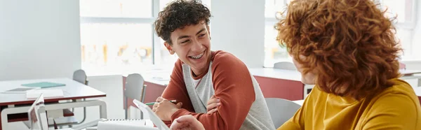 Seducente adolescente sorridente che parla con il compagno di classe vicino ai dispositivi durante la lezione in classe, banner — Foto stock