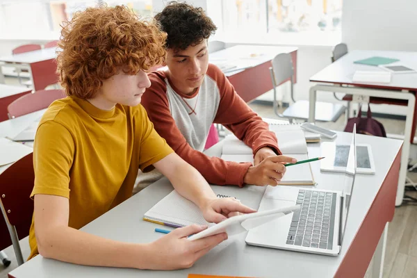 Teenage schoolboys using devices together during lesson in classroom at background in school — Stock Photo