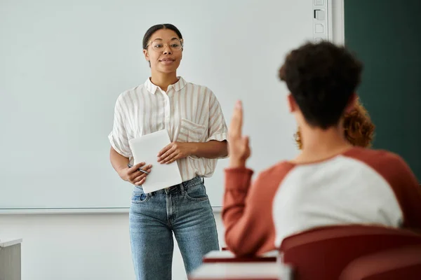 African american teacher holding digital tablet near teen schoolboy raising hand in classroom — Stock Photo