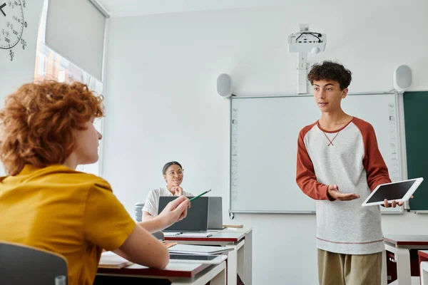 Teen schoolboy pointing at digital tablet with blank screen near classmate during lesson in class — Stock Photo