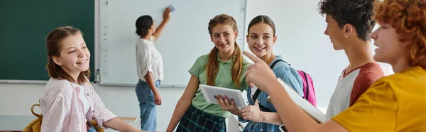 Écoliers parlant et pointant vers des amis proches et professeur afro-américain flou en classe, bannière — Photo de stock