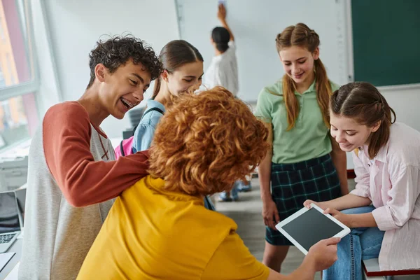 Alegre adolescente pupilos usando tableta digital con pantalla en blanco en el aula en la escuela - foto de stock