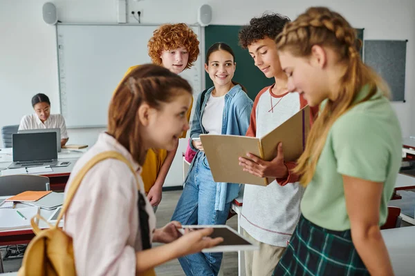 Школярка тримає блокнот біля друзів зі смартфоном і стоїть в класі в школі — стокове фото