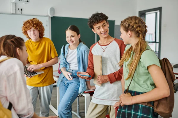 Adolescentes felices hablando en el aula, de vuelta a la escuela, compañeros de clase comunicándose durante las vacaciones escolares - foto de stock