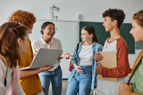 Cheerful african american teacher laughing with teenage students in classroom, back to school — Stock Photo