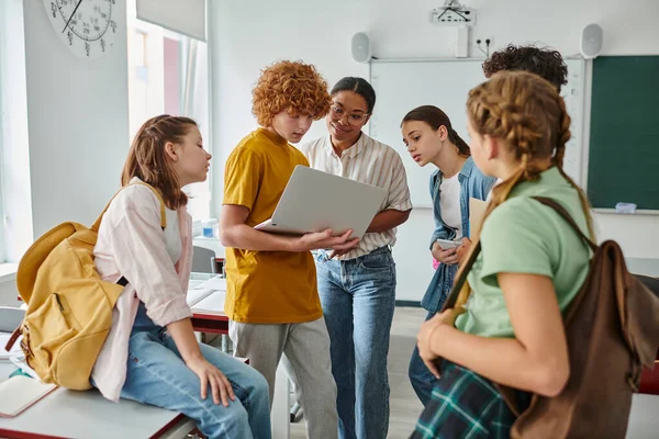 Redhead schoolboy showing laptop to african american teacher near classmates, back to school concept — Stock Photo