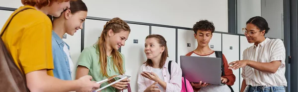 Banner, teenage students holding devices in school hallway, african american woman standing near boy — Stock Photo