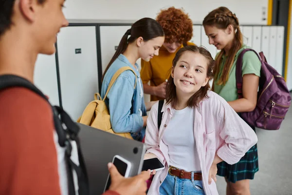 Happy girl holding smartphone and talking to teenage classmate in hallway, back to school concept — Stock Photo