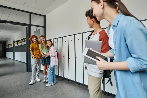 Счастливые студенты смотрят на одноклассников с устройствами в школьном коридоре, обратно к школьной концепции — стоковое фото