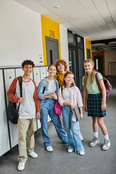 Teenage schoolkids looking at camera and standing together in school hallway, teen classmates — Stock Photo