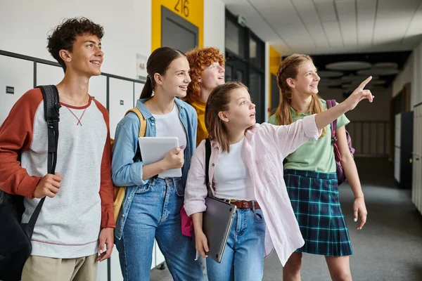 Happy teenage schoolkids looking away in school hallway, teen girl pointing with finger away — Stock Photo