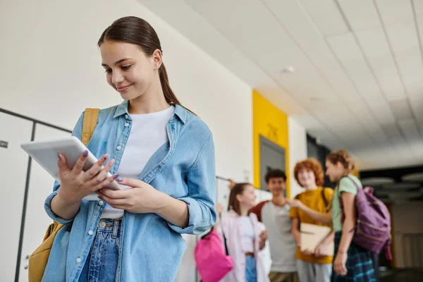 Щаслива школярка використовує цифровий планшет під час перерви в шкільному коридорі, розмиті, школярки — стокове фото