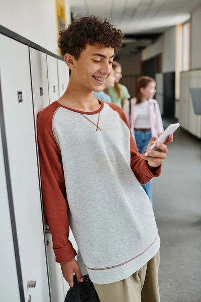 Happy schoolboy with braces using smartphone in school hallway, student during break, social media — Stock Photo