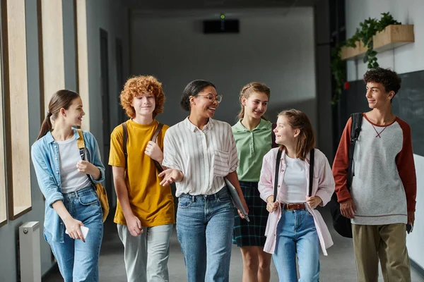Happy african american woman walking with teenage students in hallway of school, teacher and kids — Stock Photo