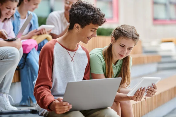 Повернутися до школи, дівчина-підліток показує цифровий планшет щасливому хлопчику, різноманітність, вчителька та студенти, розмитість — стокове фото