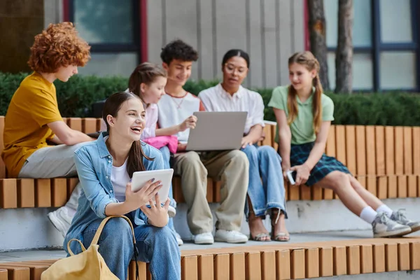 Retour à l'école, jeune fille tenant une tablette numérique et riant en plein air, e-study, diversité, étudiants — Photo de stock