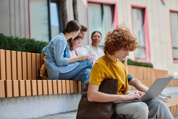 Voltar para a escola, menino ruivo encaracolado usando laptop ao ar livre, pausa, diversidade, professor e alunos — Fotografia de Stock