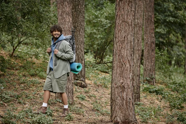 Happy young indian tourist with backpack looking away while walking in forest — Stock Photo