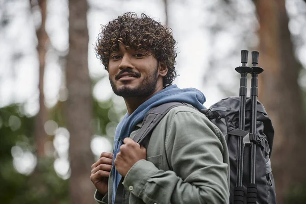 Porträt eines lächelnden indischen Wanderers mit Rucksack und Kamera im verschwommenen Wald — Stockfoto