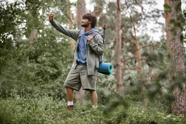 Усміхнений індійський пішохід з рюкзаком бере селфі на смартфон у розмитому лісі — стокове фото
