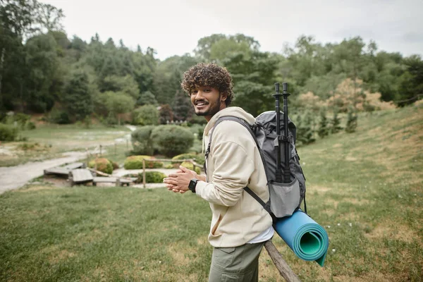 Jeune randonneur indien positif avec sac à dos regardant caméra avec paysage sur fond — Photo de stock