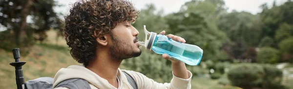 Side view of indian backpacker drinking water with landscape on background, banner — Stock Photo