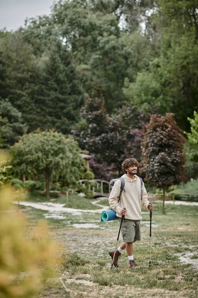Allegro zaino in spalla indiano che tiene bastoni da trekking sul sentiero nella foresta, viaggio e concetto di avventura — Foto stock