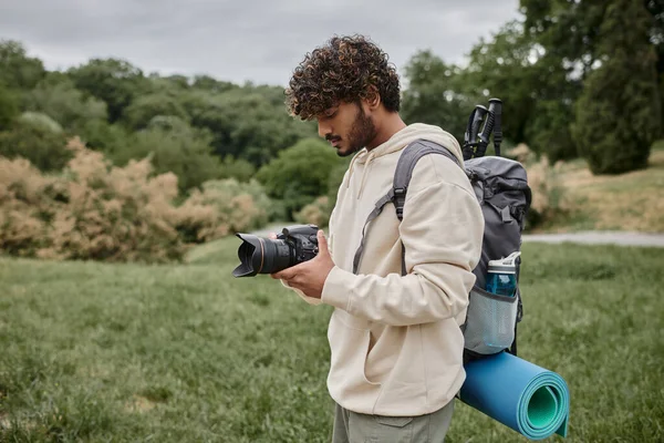 Fotógrafo indio sonriendo y sosteniendo la cámara digital en el bosque, fotografía y concepto de aventura - foto de stock