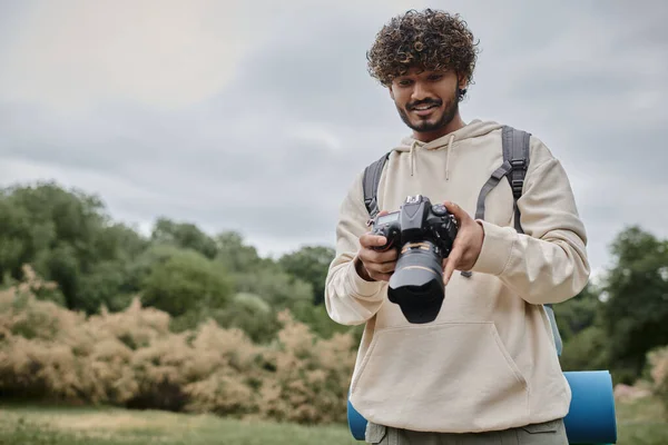 Glücklicher indischer Fotograf im Kapuzenpulli mit professioneller Kamera, Reise- und Abenteuerkonzept — Stockfoto