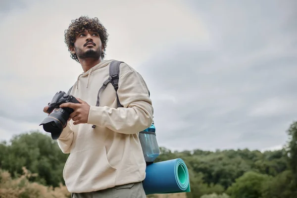 Fotógrafo indiano encaracolado em capuz segurando câmera profissional, viagem e conceito de aventura — Fotografia de Stock