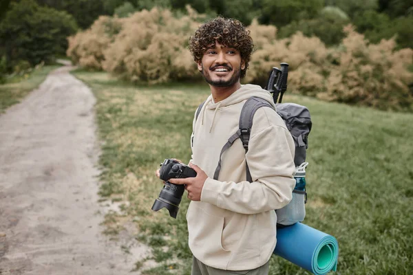 Веселий індійський фотограф з рюкзаком тримає професійну камеру, пригоди та походи — стокове фото