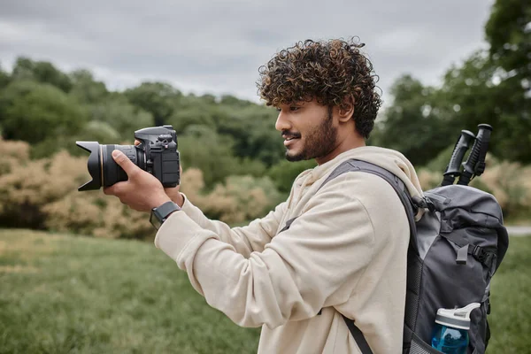 Curly indian photographer with backpack taking shot on professional camera, adventure and hiking — Stock Photo