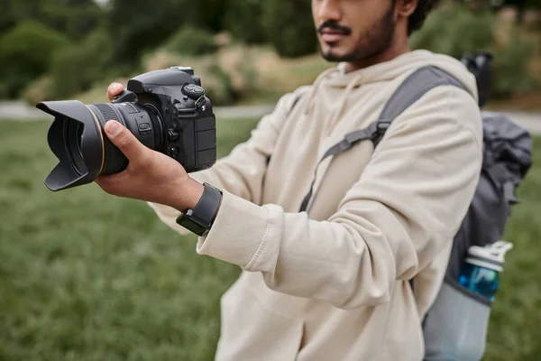 Обрезанный вид индийского фотографа с рюкзаком, снятый на профессиональную камеру, приключение — стоковое фото