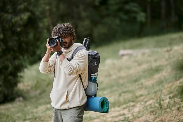 Lockiger indischer Tourist fotografiert mit professioneller Kamera, Wanderer mit Rucksack im Wald, Entdecker — Stockfoto