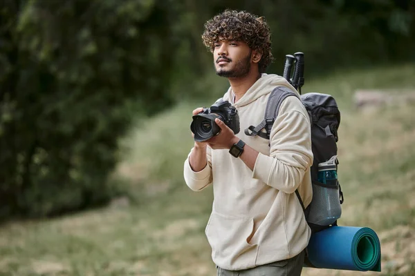 Pensivo índio turista segurando câmera profissional, caminhante com mochila na floresta, explorador — Fotografia de Stock
