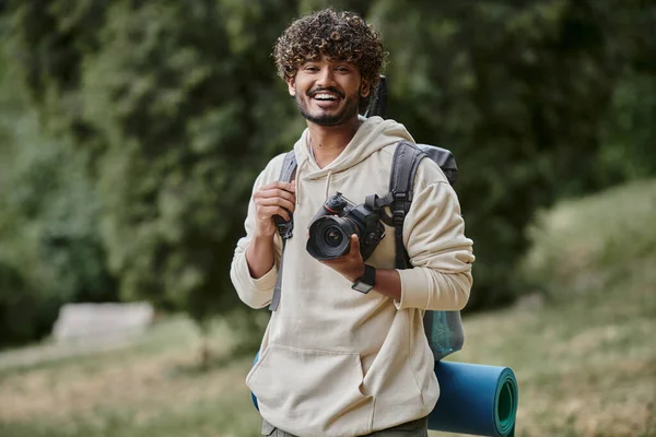 Excited indian tourist holding professional camera, hiker with backpack in forest, laughter — Stock Photo