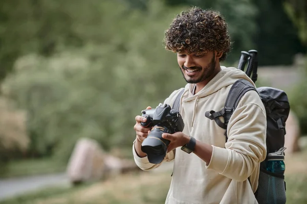 Allegro turista indiano guardando la macchina fotografica e controllando le foto, escursionista con zaino nella foresta — Foto stock