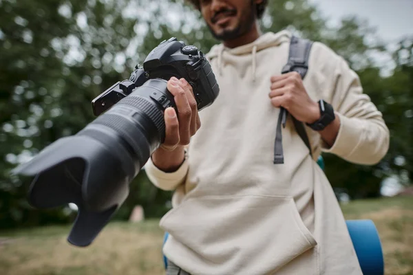 Vue recadrée de l'homme indien tenant appareil photo numérique et debout avec sac à dos dans les bois, photographe — Photo de stock