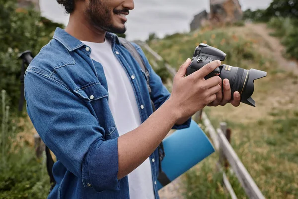 Travel and photography concept, happy indian man taking photo on digital camera in natural place — Stock Photo