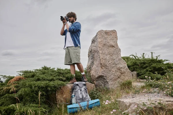 Fotografía y concepto de la naturaleza, mochilero indio tomando fotos en cámara digital y de pie sobre roca - foto de stock