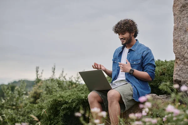 Digital nomad concept, cheerful indian freelancer having video call on laptop in natural location — Stock Photo